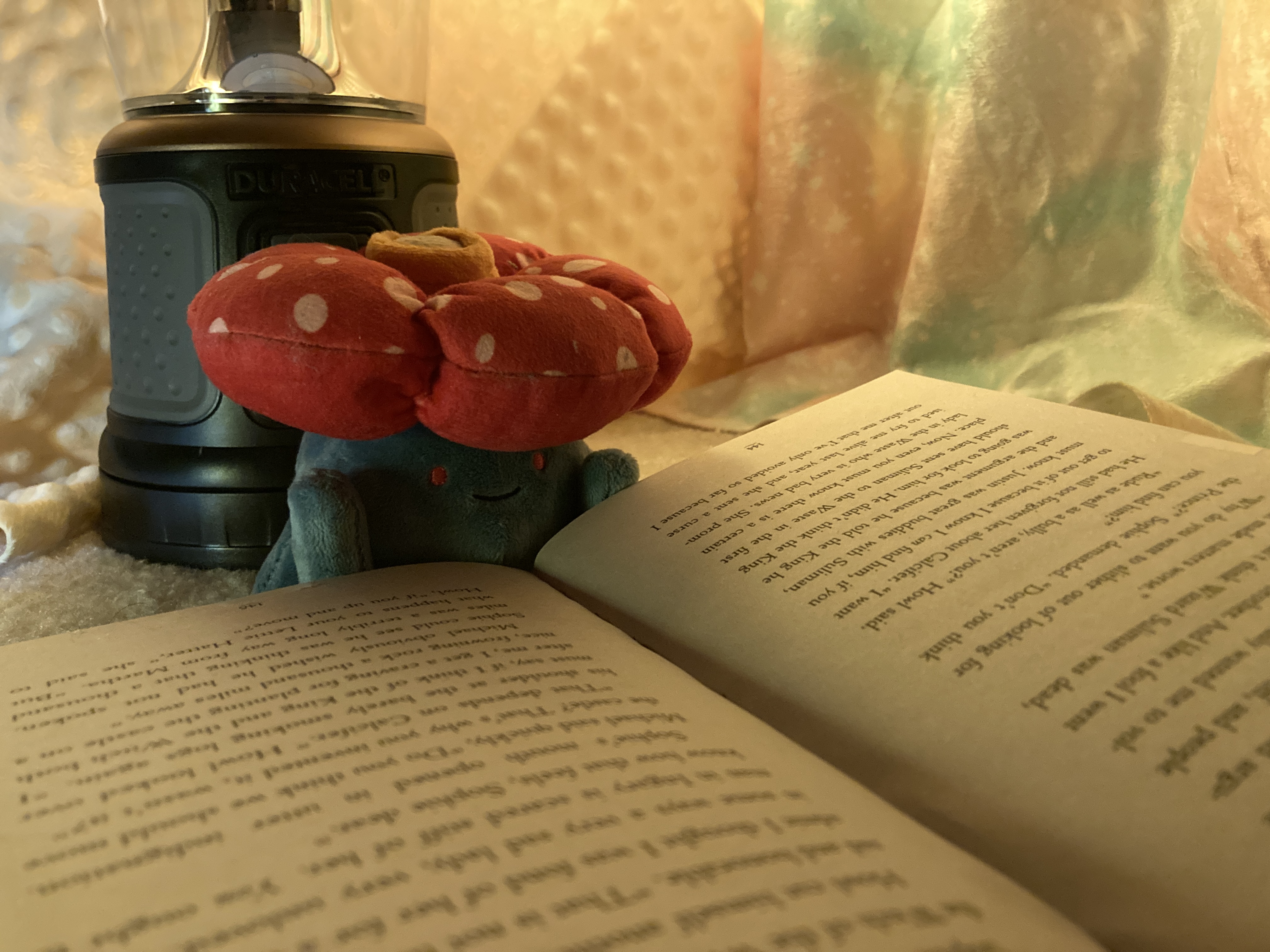 A plush Pokemon, Vileplume, reading a book in a blanket fort by a lamp.