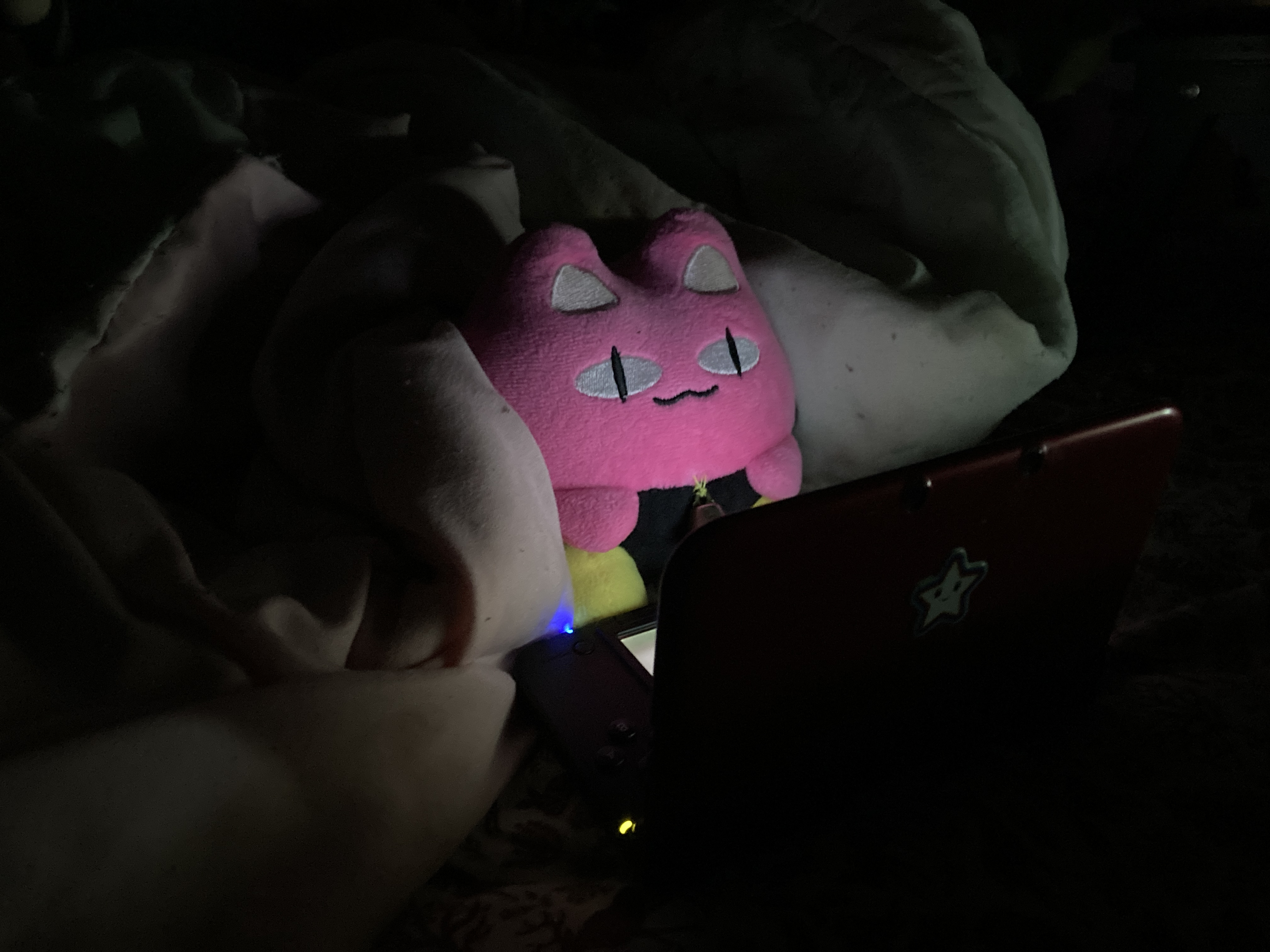 An ItemLabel Dinkle in bed playing on a 3DS.