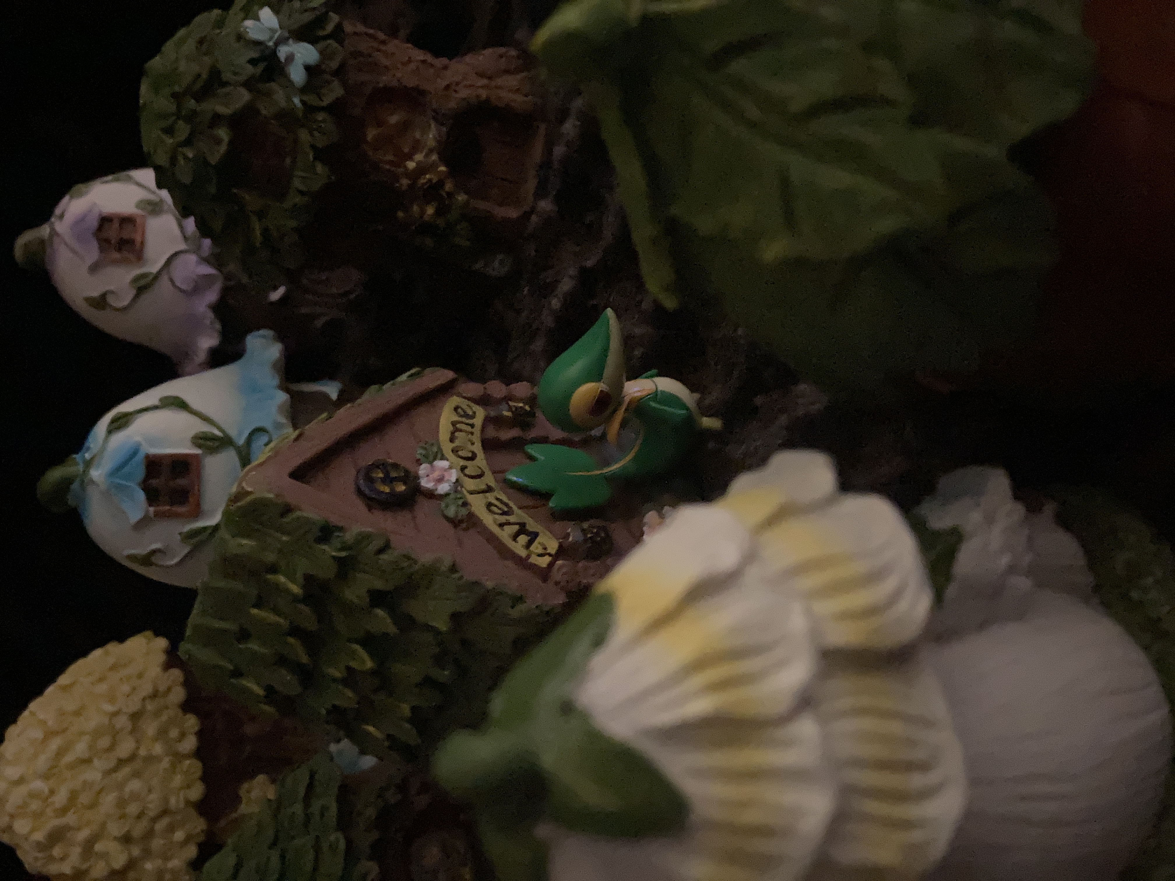 A Pokemon figurine, Snivy, standing outside of a miniature fairy neighborhood.